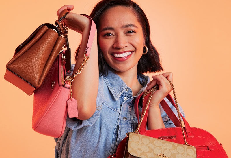 Photo of a smiling person holding several handbags